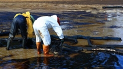 Professional team and volunteer wearing PPE clean up dirty of oil spill on the beach, oil slick washed up on a sand beach