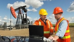 Two men in hard hats on an oil & gas site with oil pump in the background