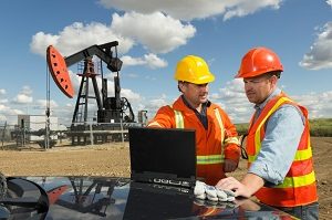 Two men in hard hats on an oil & gas site with oil pump in the background