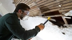 Person in mask tearing out ceiling boards with a crowbar