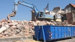 Excavator loading debris into a blue dumpster