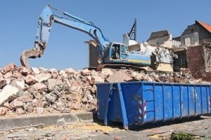 Excavator loading debris into a blue dumpster