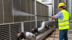 Man in hard hat power washing machinery