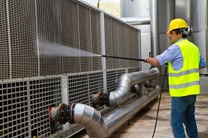 Man in hard hat power washing machinery