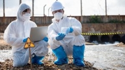 Environmental contractors in protective suits kneeling by water