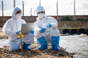 Environmental contractors in protective suits kneeling by water