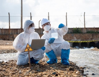 Professionals in protective gear crouched near a hazard sign