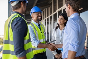 Smiling engineer shaking hands at construction site with happy architect. Handshake between cheerful african construction manager with businessman at bulding site. Team of workers with architects and contractor conclude an agreement with safety uniform.