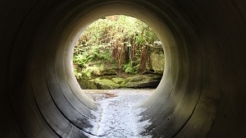 View through a round concrete tunnel carrying a stream beneath a road