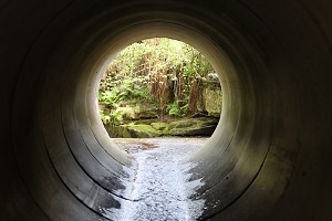 View through a round concrete tunnel carrying a stream beneath a road